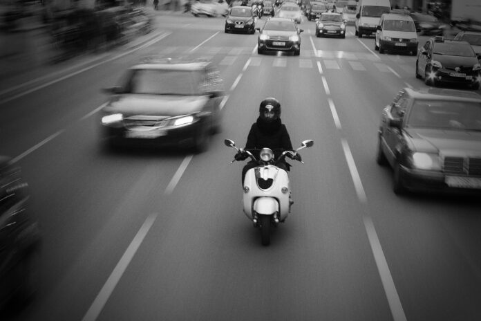 Ein Motorroller im Straßenverkehr zwischen Autos, die mehrspurig in dieselbe Richtung fahren.