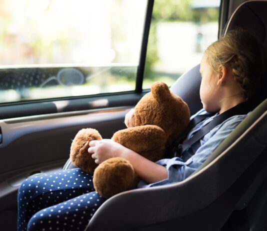 Ein Mädchen sitzt in einem Kindersitz im Auto und schläft. Sie hält einen Teddybären dabei.