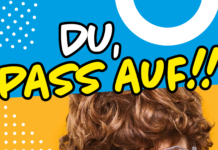 Ein Bub mit lockigen Haaren und Brille zeigt mit zusammengekniffenen Augen in Richtung der betrachtenden Person. Der Bildtext: "DU, PASS AUF!!"