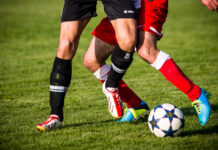 Zwei Spieler von der Hüfte abwärts in unterschiedlich färbigen Dressen im Zweikampfduell um den Fußball.