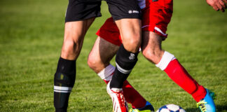 Zwei Spieler von der Hüfte abwärts in unterschiedlich färbigen Dressen im Zweikampfduell um den Fußball.