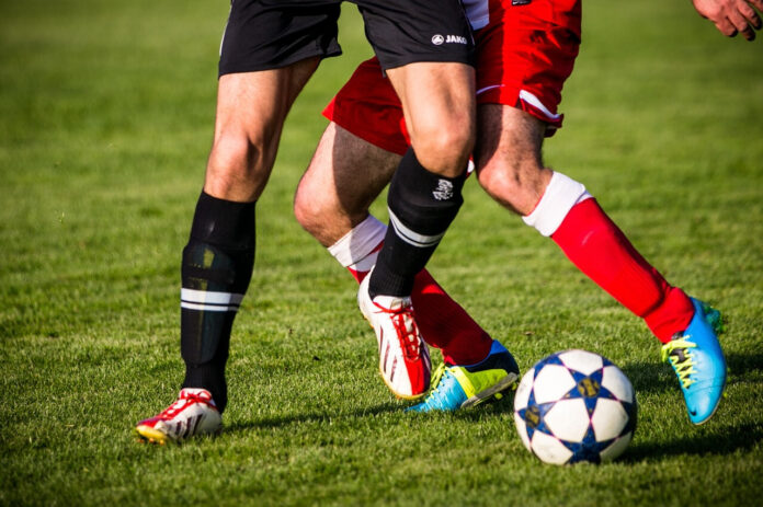 Zwei Spieler von der Hüfte abwärts in unterschiedlich färbigen Dressen im Zweikampfduell um den Fußball.