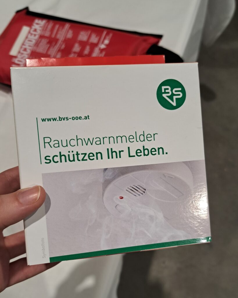 Ein Rauchwarnmelder in der Verpackung mit Logo der BVS Oö. Der Text darauf: "Rauchwarnmelder schützen Ihr Leben."